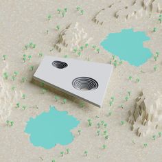 an electronic device with two holes in the middle surrounded by small green plants and rocks