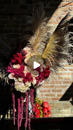 an arrangement of flowers and feathers is displayed in front of a brick wall with a video player