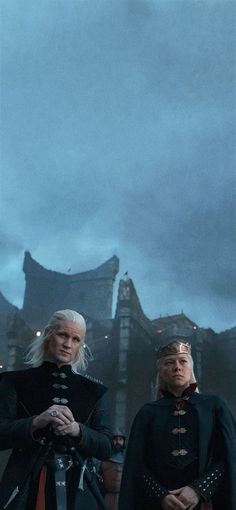 two men standing next to each other in front of a building with dark clouds behind them