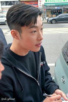 a young man sitting in front of a parked car