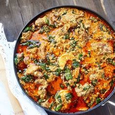 a pan filled with meat and vegetables on top of a wooden table next to a white napkin