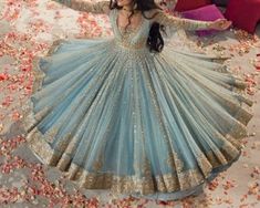 a woman in a blue and gold dress standing on a bed of rose petals with her arms outstretched