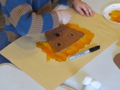 a young boy is making a paper lion craft with orange and yellow paint on it