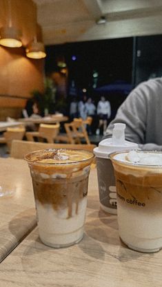 two iced coffees sitting on top of a wooden table next to eachother