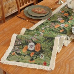 two placemats with flowers on them sitting on a wooden table next to plates and utensils