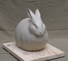 a white sculpture of a rabbit sitting on top of a piece of plywood wood