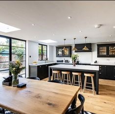 an open kitchen and dining room area with wooden table, bar stools, black cabinets and windows