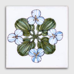 a white tile with blue flowers and green leaves on it's center, in the shape of a flower