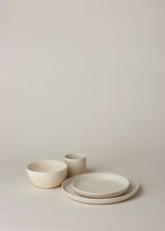 two white plates and one bowl are on the table next to each other, against a gray background