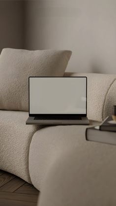 a laptop computer sitting on top of a white couch next to a book and cup