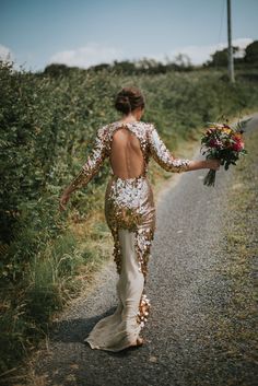 the back of a woman's dress as she walks down a road with her bouquet in hand