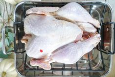 raw chicken sitting on top of a metal pan next to white pumpkins and leaves