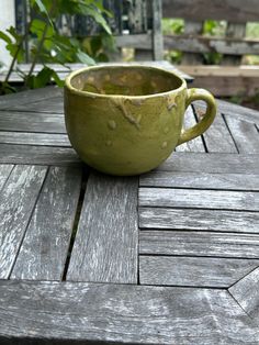 a green cup sitting on top of a wooden table next to some plants and bushes