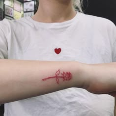 a woman's arm with a red rose tattoo on her left arm and a heart in the background