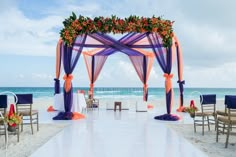 an outdoor wedding setup on the beach with blue and orange draping, flowers and chairs