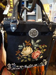 a black purse with flowers on it hanging from a rack in a room filled with other items