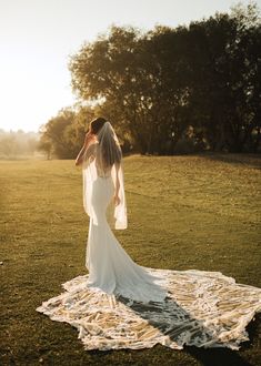 a woman in a wedding dress is standing on the grass with her veil over her head