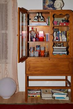 a wooden cabinet filled with lots of books and knick - knacks next to a window