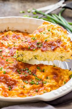 a piece of lasagna being lifted from a casserole dish with green onions