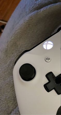 a close up of a white controller on a gray blanket with a wooden floor in the background