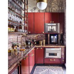 a kitchen with red cabinets and marble counter tops, gold trimmings on the walls