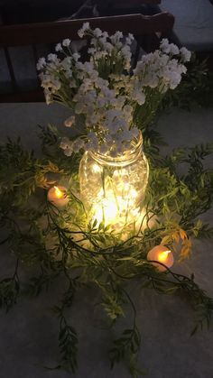 flowers and candles are lit in a jar on the ground with greenery around it