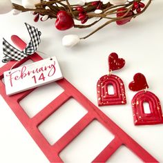 a pair of red earrings sitting on top of a ladder next to a sign that says happy valentine's day