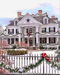 a large white house decorated for christmas with wreaths and lights on the front gate