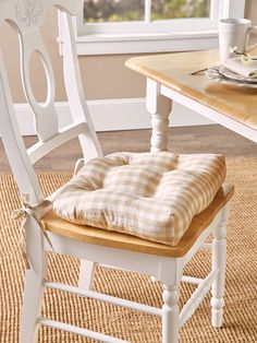 a chair with a cushion on top of it in front of a table and window