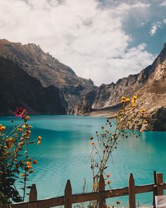 a wooden fence sitting next to a lake filled with water and mountains in the background