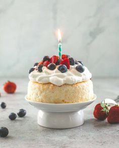 a birthday cake with strawberries and blueberries on top, sitting on a white pedestal