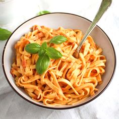 a white bowl filled with pasta and topped with basil