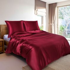 a bed with red sheets and pillows in front of a window