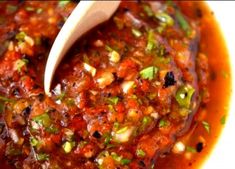 a wooden spoon in a bowl filled with sauce and garnishes on top