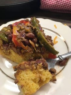 a white plate topped with a piece of cake and beans on top of cornbread