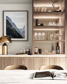 an open book is sitting on a table in front of a shelf with wine glasses