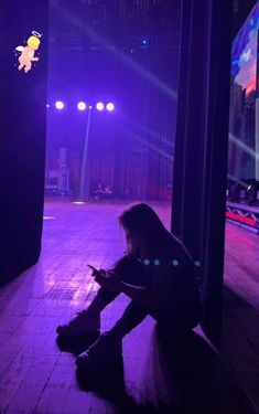 a woman sitting on the floor in front of a stage with purple lights and spotlights