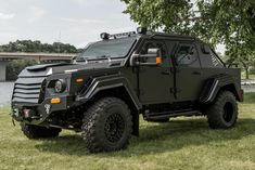 an armored vehicle parked in the grass near a tree and bridge on a sunny day