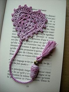 an open book with a crocheted pink tassel on top of it and a purple tassel hanging from the end