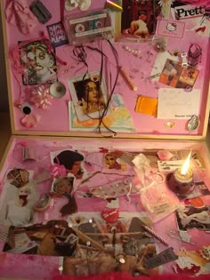 an open pink suitcase filled with assorted items on top of a wooden table next to a lit candle