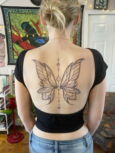 a woman with a butterfly back tattoo on her upper and lower back, standing in front of a wall