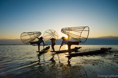 three people on small boats in the water with their backs turned to the camera, at sunset