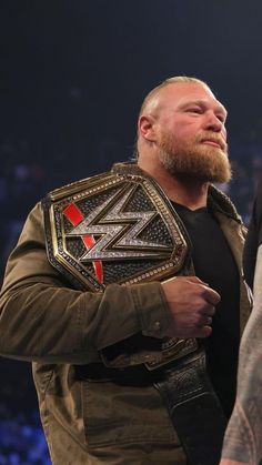 a man with a beard standing next to another man wearing a leather jacket and holding a wrestling belt