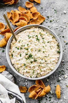 a white bowl filled with dip surrounded by tortilla chips on a gray surface