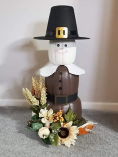 a fake scarecrow is sitting on the floor next to some flowers and leaves in front of a wall