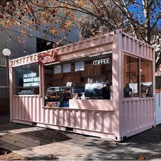 a pink coffee shop sitting on the side of a road next to a tree with lots of leaves