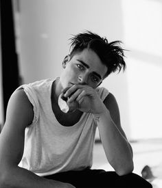 a black and white photo of a young man sitting on the floor with his hands to his face