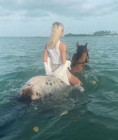 a woman riding on the back of a horse in the ocean next to a brown horse