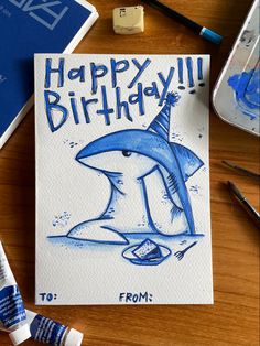 a happy birthday card with a shark on it and some markers next to the card