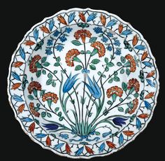 a white plate with blue and orange flowers on the bottom, surrounded by green leaves